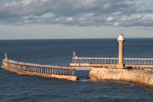 A  bridge spanning a body of water, leading to a coastline with Whitby Lighthouse in Yorkshire England
