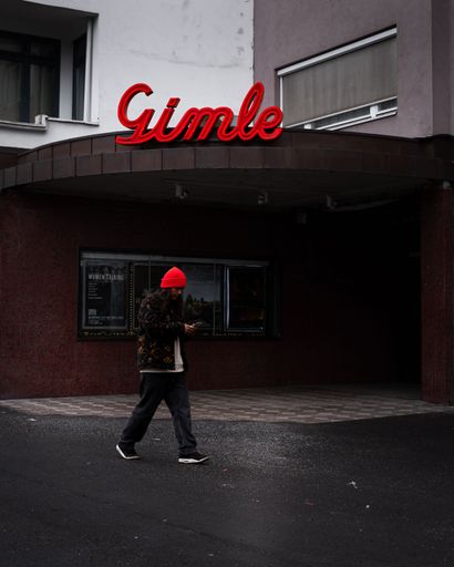 A young man is walking outdoors in the rain, using his mobile phone at the Gimle cinema
