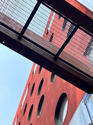 A low angle, vertical shot of a pedestrian bridge close to a red building with circular windows