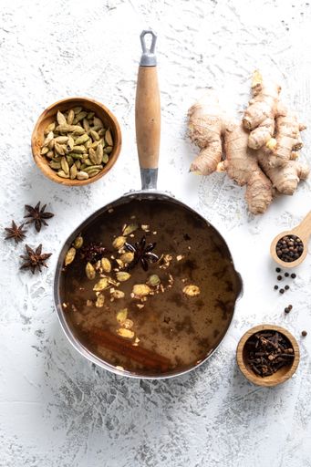 Top View of chai Latte in a pot with spices around to it: cloves, cardamom and ginger