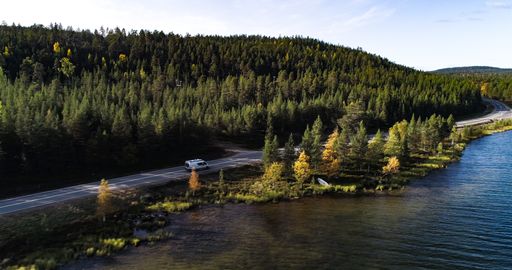 Cars on the coast of a lake Inarinjarvi in Lapland. Aerial, drone shot, following a camper on route e75, in middle of fall color forest, in Finland
