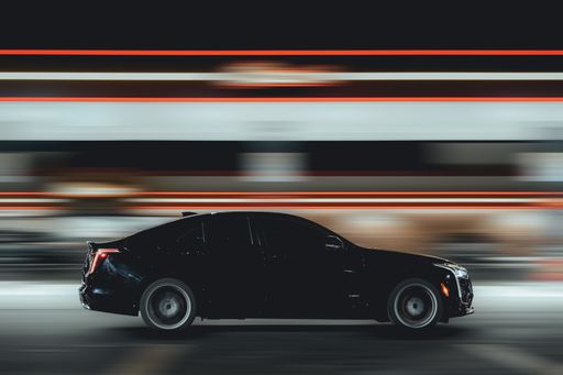 A black car traveling on a road at night, with motion blur in the background.