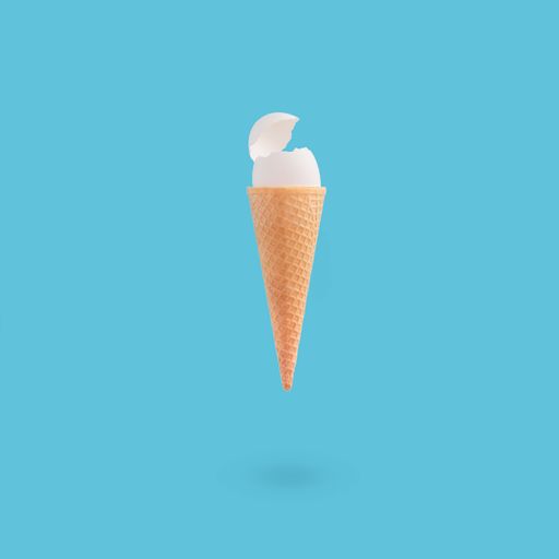 A vertical shot of a cracked white egg on an ice cream cone on a blue background