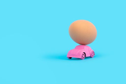 A pink toy car carrying a chicken egg on a blue background