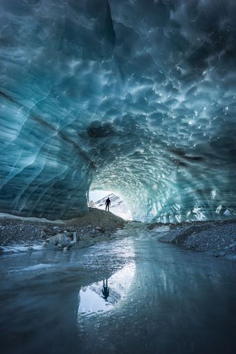 Landscape view of a silhouette reflecting in the melting ice of an ice cave in Furgg glacier in Zermatt, with blue shades and textures