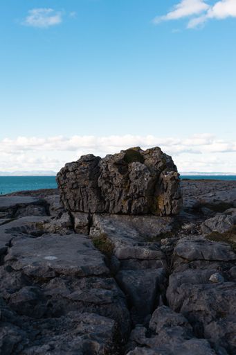 A large rock in the center of a rocky terrain, surrounded by tranquil blue waters. Cliffs of Moher.