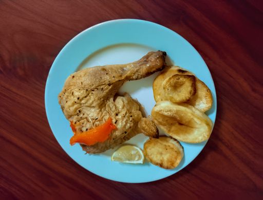 An overhead shot of a traditional cooked chicken leg and roasted Spanish potatoes on a plate on a wooden background