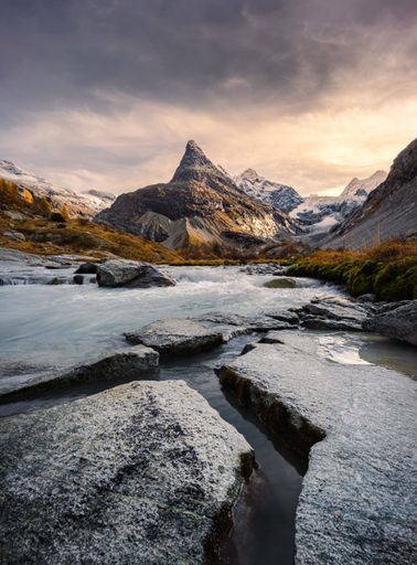 Landscape autumnal view of the Mont Mine and Ferpecle glacier at sunset with cracks in the foreground rocks and a river