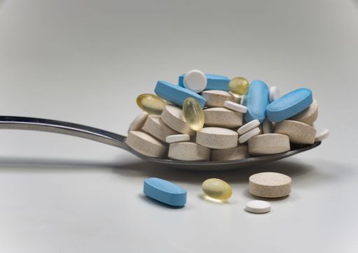 A stainless steel spoon with a variety of blue and yellow capsules on top of each other.