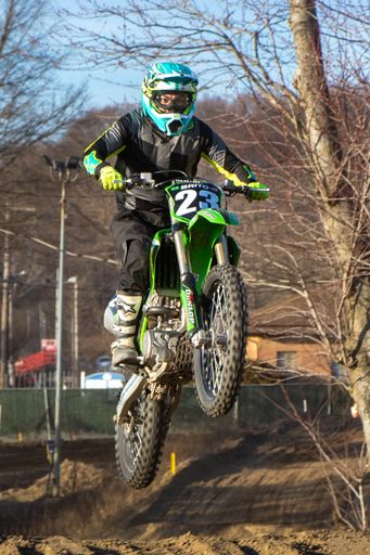 A young adult man riding an off-road dirt bike performing an airborne jump over a dirt terrain