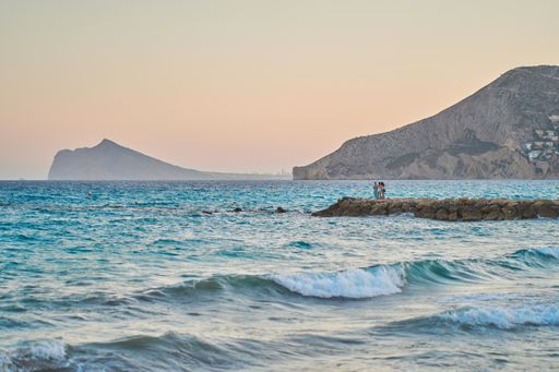 A beautiful shot of people standing on a beach mole surrounded by turquoise water in the seashore