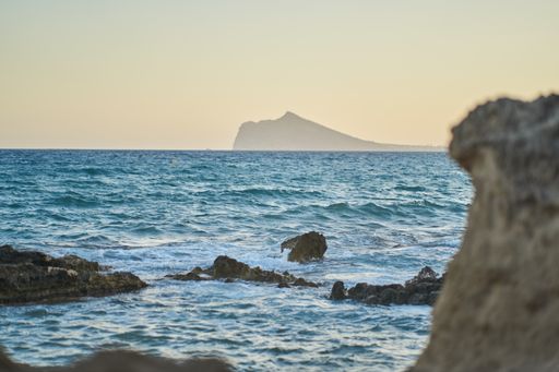 A beautiful shot of turquoise water splashing on the rocky seashore with a silhouette of mountain cliff on the background