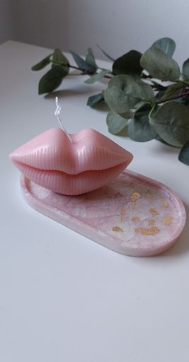 A pink lip-shaped candle resting on a white and pink abstract background