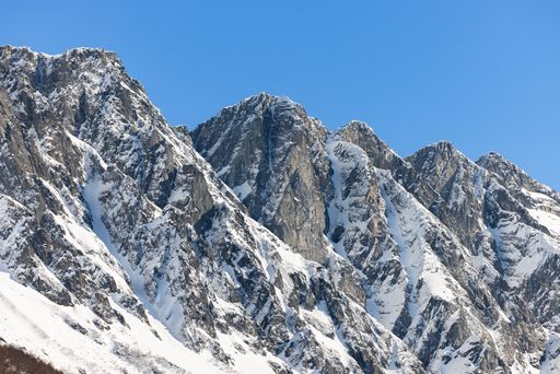 A majestic mountain range blanketed in freshly fallen snow under a brilliant blue sky.