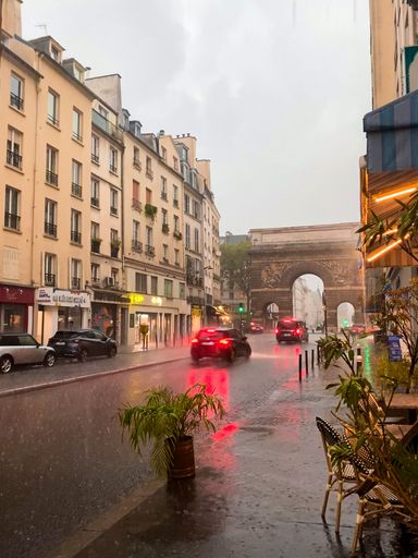 An urban street scene in a rainy weather with the triumphal arch of Porte Saint-Denis visible