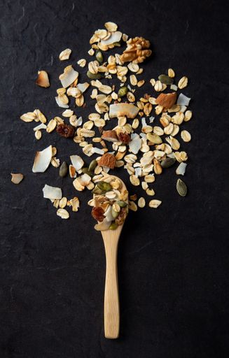 A vertical shot of healthy and delicious spooned muesli on a black background