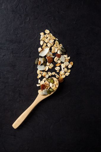 A vertical shot of healthy and delicious spooned muesli on a black background