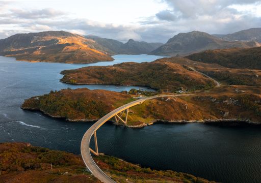 Aerial view of a winding road snaking through a picturesque landscape of serene water and majestic mountains
