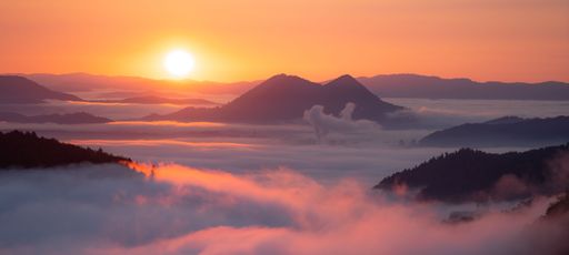 An awe-inspiring view of the sun rising over the majestic mountains in with a backdrop of wispy clouds at sunset