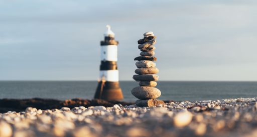 A scenic view of the Penmon Point Lighthouse with a tower of rocks at the shore in the foreground