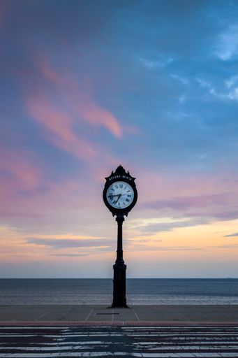 An antique clock tower stands at the shoreline of Revere Beach, illuminated by the beautiful golden hues of a stunning sunset