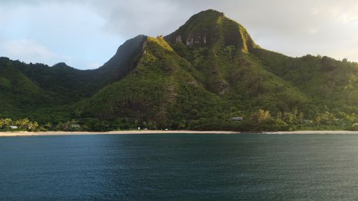 An idyllic beach view featuring a small island in the background framed by majestic mountains