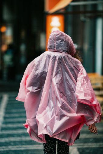 A young female wearing a pink raincoat walking down a city street