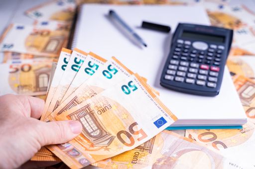 A closeup shot of 50 Euro bills, a calculator and an empty notebook on a wooden surface