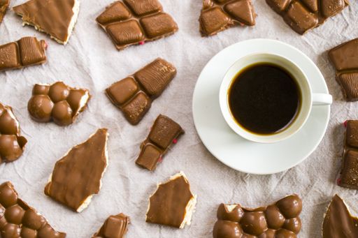 A top view of a cup of black espresso coffee and chocolate bars on a white cloth background
