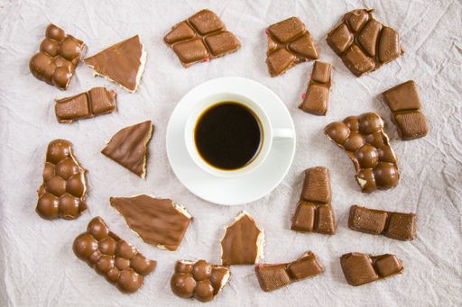 A top view of a cup of black espresso coffee and chocolate bars on a white cloth background