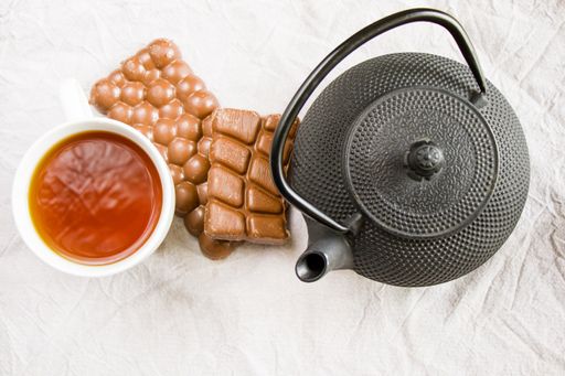 A cup of tea, an iron teapot and chocolate bars on a white cloth background