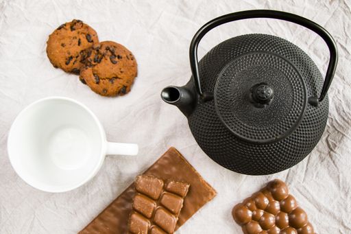 An empty cup, an iron teapot, cookies, and chocolate bars on a white cloth background