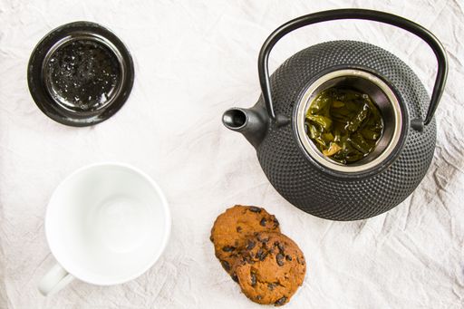 A flat lay of cup of tea, iron teapot and cookies on white cloth background - morning food and drink, sweet pastry dessert with chocolate and nuts