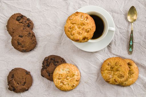 A top down shot of cup of black espresso coffee, a spoon and cookies on white cloth background, morning breakfast