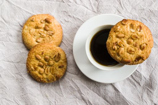 A top down shot of a cup of black espresso coffee and cookies with nuts on white cloth background, morning breakfast