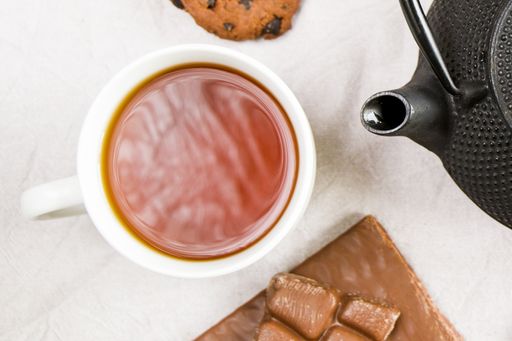 A closeup top down shot of cup of tea, iron teapot and cookie on white cloth background