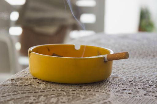A high-resolution, close-up image of a yellow ashtray with a single cigarette placed in the center