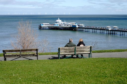 Llandudno Wales UK March 2023 two middle age adults sat on a park bench over looking the pier at Llandudno