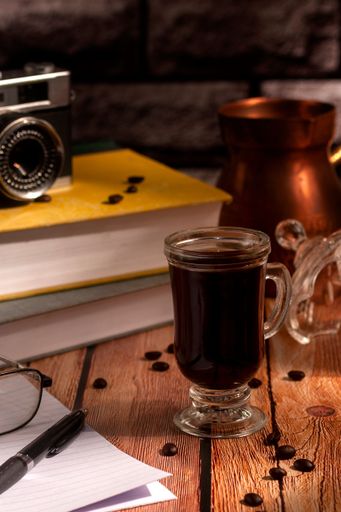 A cup of hot coffee on the table with a film camera and textbooks on it