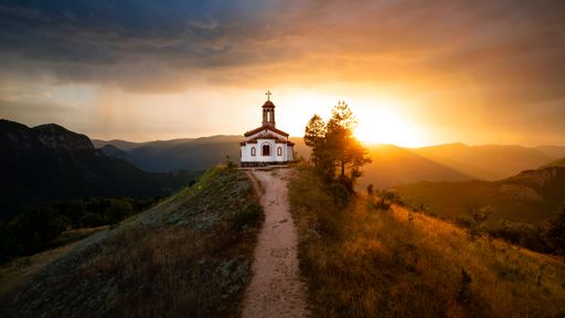 An amazing sunset captured from the air, showing a small Orthodox Christian chapel on the top of a small hill, with spectacular clouds in the backdrop