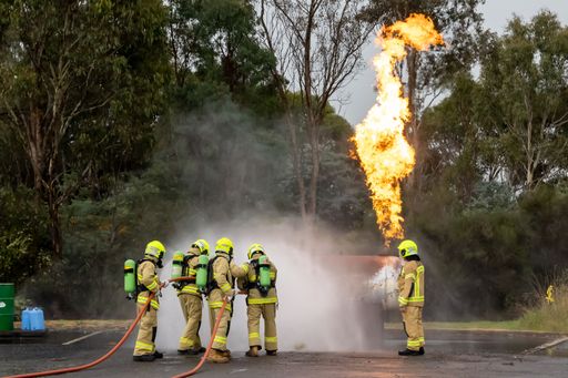 A group of firefighters in a parking lot are engaged in extinguishing an active blaze.