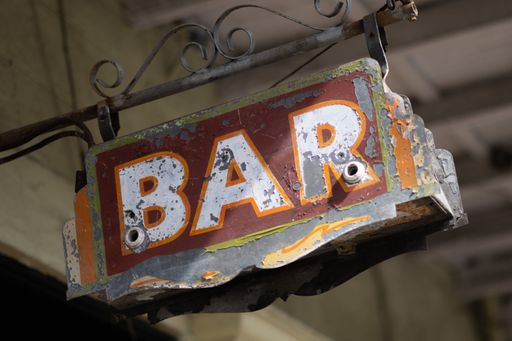 A distressed, rusty metal pole displays a faded sign that reads 'bar'.