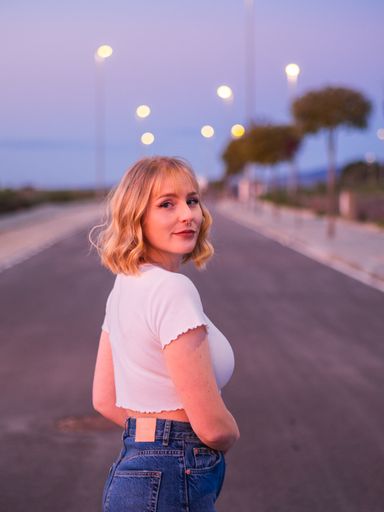 A vertical shot of a blonde Caucasian woman from Spain standing in the middle of a road in a white crop top