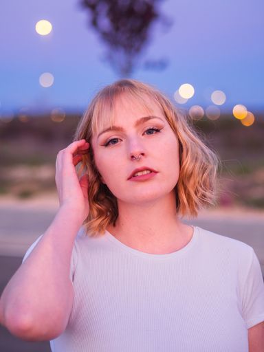 A shallow focus shot of a beautiful blonde caucasian female with a white shirt touching her hair