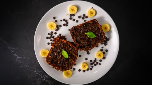 A top view of sliced chocolate cake with chips and banana on a white plate topped with green leaves