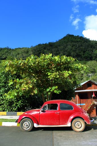 A vertical shot of a red vintage car parked outside a house in Oxapampa, Peru