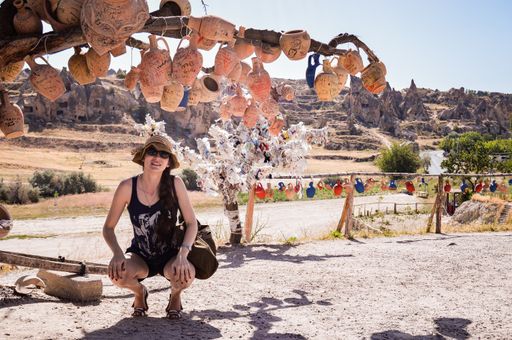 An Uruguayan female tourist squatted under the tree with clay jugs near Goreme open-air museum In Cappadocia, Turkey
