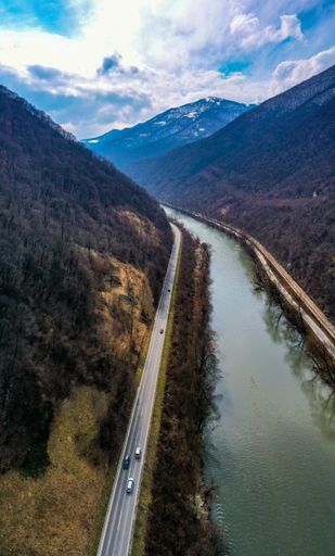 A vertical shot of a canal surrounded by hills under the sunlight and a blue cloudy sky