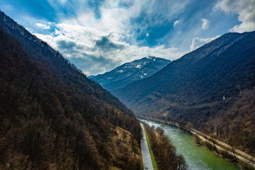 A landscape of a canal surrounded by hills under the sunlight and a blue cloudy sky