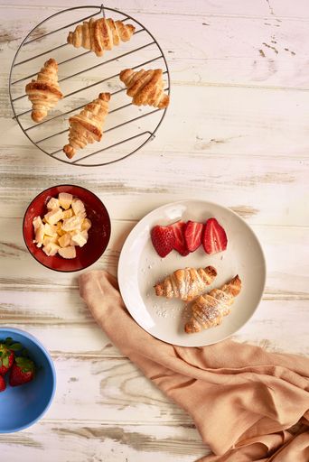 A breakfast set with freshly-baked croissants, and a handful of ripe strawberries on a table